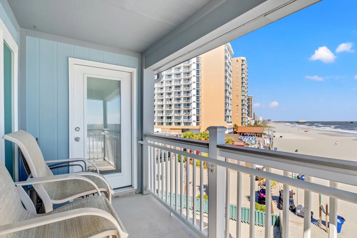 A private balcony with comfortable seating overlooks the beach, with ocean waves and a tranquil shoreline in view. The space is ideal for sipping drinks, catching sunrises, or simply enjoying the gentle sea breeze just steps from the main living area.