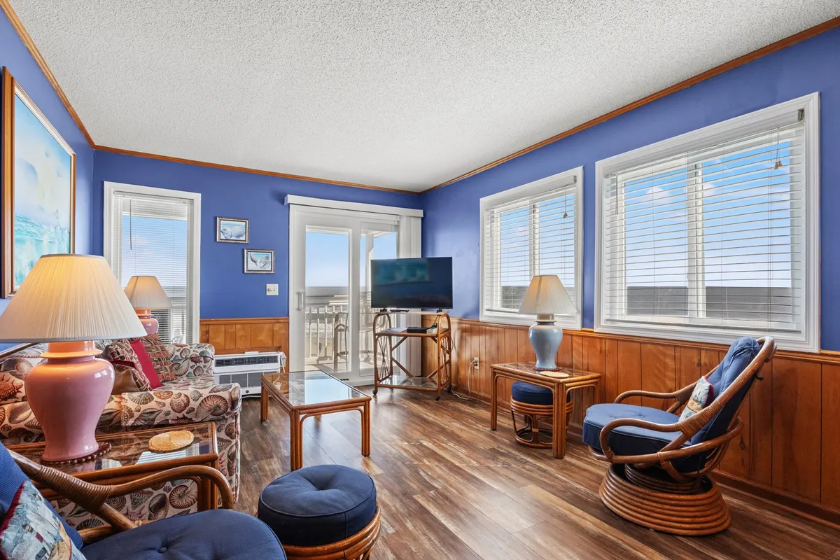 A bright, cheerful living area featuring a colorful couch, large windows that usher in sunrise views, and wooden accents for a fresh, revitalized feel. A TV and decorative lamps suggest a space tailored for both day and evening lounging, reading, or lively conversations.