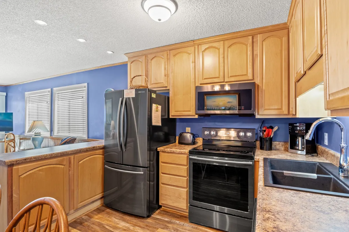 A closer perspective of the kitchen, highlighting the kitchen appliances, wooden cabinets, and countertop. The warm lighting and practical setup evoke a welcoming and homely environment perfect for meal prep and gathering.
