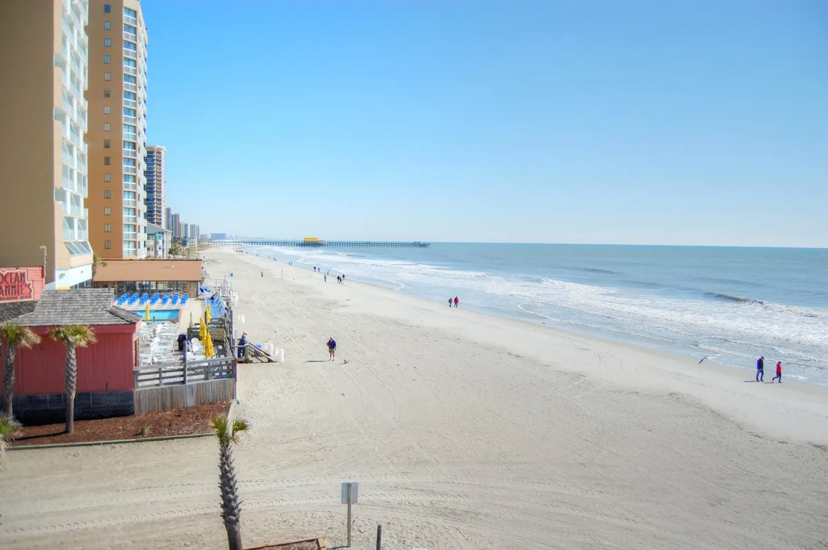 A sweeping view of the ocean, sandy beach, and iconic pier set against high-rise buildings, offering a sense of both relaxation and proximity to local attractions. The scene transitions smoothly from energetic nightlife to tranquil downtime by the sea.